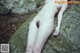 A naked woman laying on a rock in the woods.